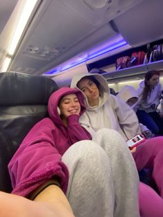 two people sitting on an airplane, one in a pink robe and the other in a white hat