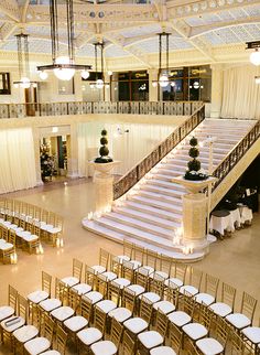 an indoor wedding venue with gold chairs and white tablecloths set up for the ceremony