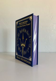 a book that is sitting on top of a white table with a blue cover and gold trim