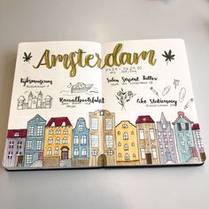 an open notebook with the words amsterdam written in gold on it and houses drawn by hand