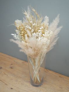 a vase filled with lots of white flowers on top of a wooden table next to a wall