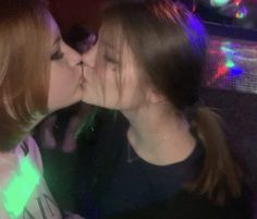 two women are kissing each other in front of a neon light background at a party