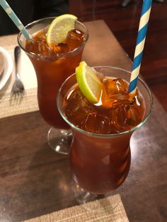 two glasses filled with drinks sitting on top of a wooden table next to each other