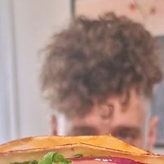 a close up of a sandwich with lettuce and tomato on it in front of a man's face