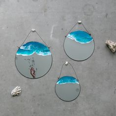 three circular mirrors hanging on the side of a cement wall next to shells and seashells