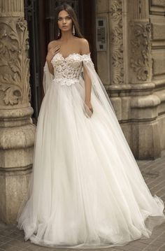 a woman in a white wedding dress standing on the street with her hand on her shoulder