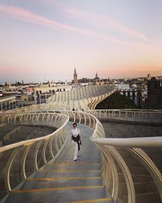 a woman is walking down some stairs in a city at sunset or sunrise with the sun setting behind her