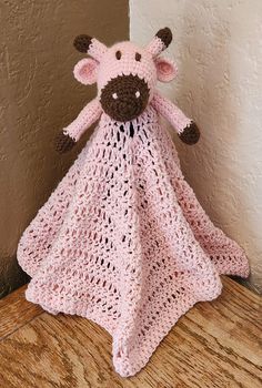 a pink crocheted cow blanket sitting on top of a wooden table next to a wall