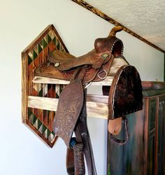 two saddles are hanging on the wall next to a wooden rack with several different types of saddles