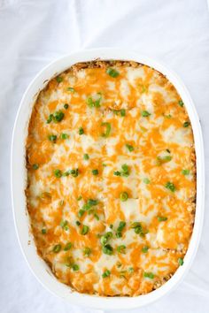 a casserole dish with cheese and green onions in it on a white cloth