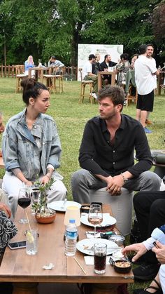 four people sitting around a table with food and drinks on it in a park setting