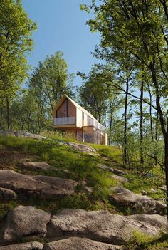 a house on top of a hill surrounded by trees and rocks in the grass,