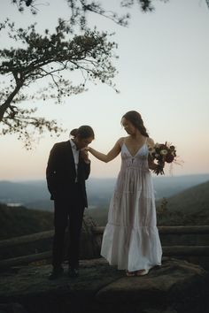 a bride and groom holding hands on top of a hill overlooking the mountains at sunset