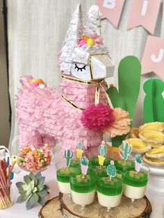 a table topped with desserts covered in pink and green frosted cake next to an alpaca