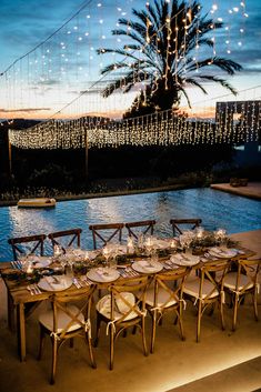 an outdoor dinner table set up with place settings and string lights strung from the ceiling