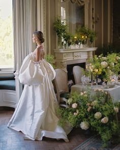 a woman in a wedding dress standing next to a table with flowers and candles on it