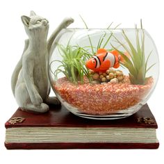 an aquarium with fish, plants and rocks in it next to a cat figurine