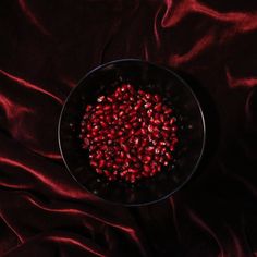 pomegranate in a black bowl on a red satin tablecloth, viewed from above