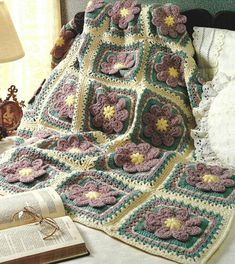 a crocheted granny blanket on a bed next to an open book and lamp