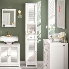 a bathroom with green walls and white furniture, including a pedestal sink and cabinet in the center