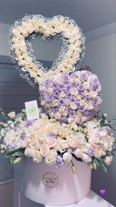 a white and purple flower arrangement in a heart shaped box on top of a table