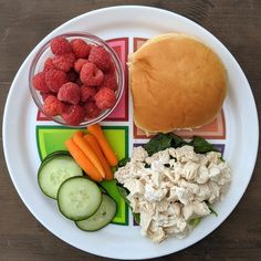 a white plate topped with a sandwich and veggies next to a bowl of raspberries