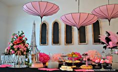 the table is set up with pink umbrellas and desserts in front of it