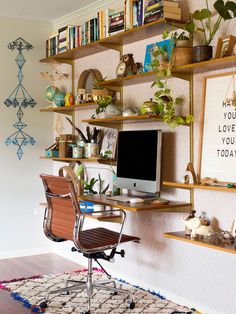 a computer desk sitting on top of a wooden chair in front of a book shelf filled with books