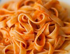 a bowl filled with pasta and sauce on top of a wooden table next to a fork