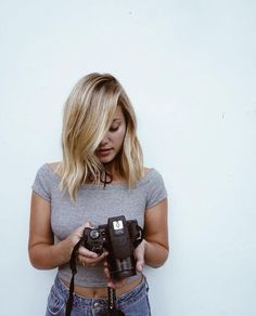 a woman holding a camera in her hands and looking down at the camera with one hand