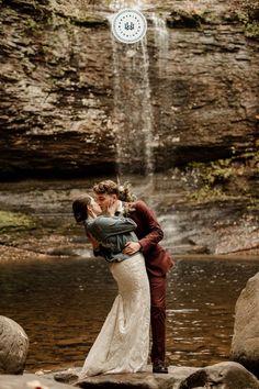 a bride and groom kissing in front of a waterfall with a clock hanging above them