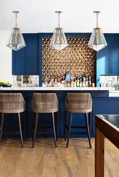 a kitchen with blue cabinets and bar stools in the center, along with three hanging lights