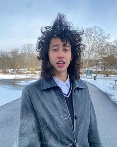 a young man with curly hair standing in the snow