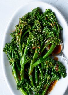 a white plate topped with broccoli covered in seasoning next to a bowl of sauce