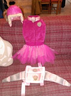 a pink dress and hat sitting on top of a red couch next to stuffed animals