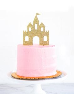 a pink and gold cake with a castle topper sitting on it's side