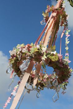 a bunch of flowers hanging from the side of a tall pole with ribbons and bows attached to it