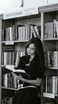 a woman sitting in front of a bookshelf holding an open book and looking at it