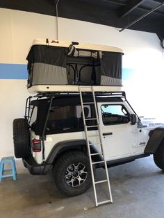 a white jeep parked in a garage with a ladder up to it's roof