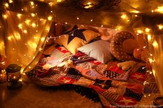 a bed covered in lots of lights next to a teddy bear on top of it