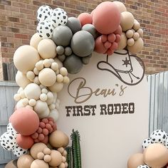 a sign that has balloons all over it and some cactus in front of it with the words bau's first rodeo written on it