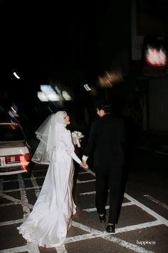 a bride and groom walking across the street at night