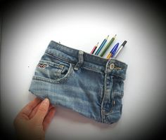 a pencil holder made out of jeans with colored pens in the pocket and one person's hand holding it