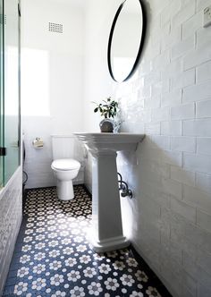 a white toilet sitting next to a sink in a bathroom under a round mirror on the wall