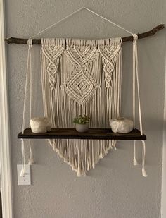 a macrame hanging on a wall with two white vases next to it