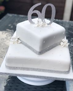 a white square cake with silver numbers and flowers on the top is sitting on a table