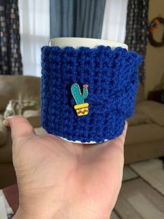 a hand holding a coffee cup with a crocheted cactus pin on the side