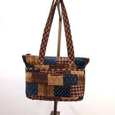 This Multi-Colored, Multi-Patterned Shoulder Bag Is Compact But Very Roomy. Six Outer Slip Pockets Surround The Bag. Three Inner Slip Pockets And One Large Inner Zip Pocket. Tan Colored Zip Closure With Ribbon. Sturdy Bag With Brass Metal Feet. Americana Themed Colors And Patterns In Neutral Brown Tones With Navy And Dark Red. Quilted Cotten. Outer Fabric Of Patchwork With Plaid And Dainty Floral Patterns. Inner Fabric Navy With Small White Flowers. Bag Measures 8" Tall X 12" X Wide X 3" Deep. S Everyday Brown Patchwork Shoulder Bag, Casual Brown Quilted Bag, Casual Brown Patchwork Bag, Fabric Navy, Small White Flowers, Brown Tones, Classic American, Brass Metal, Floral Patterns