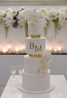 a three tiered wedding cake with white flowers and gold trimmings on top