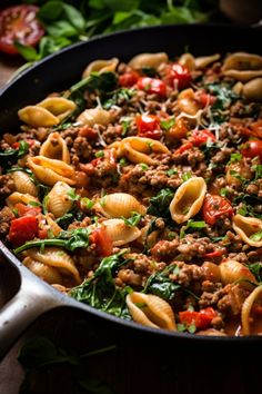 a skillet filled with pasta, meat and spinach on top of a wooden table